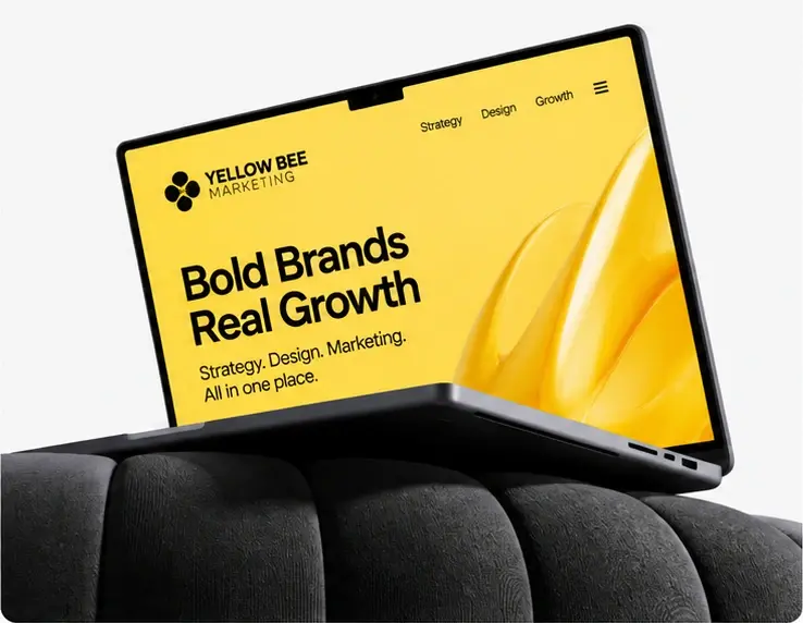 A laptop on a black cushioned surface displaying the yellow Yellow Bee Marketing website with Bold Brands Real Growth on screen.