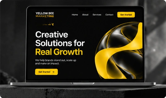 A laptop displaying the Yellow Bee Marketing website with black and yellow abstract artwork.